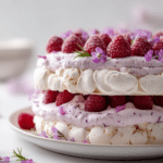 Close-up of a Raspberry-Lavender Cloud Dacquoise topped with whipped cream, fresh raspberries, and edible flowers