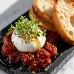 Burrata with tomato confit served with microgreens and toasted bread.